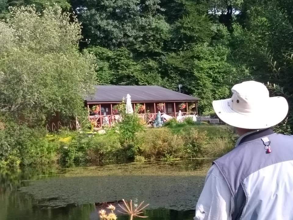 An angler in a sun hat looking across a lake to the log cabins