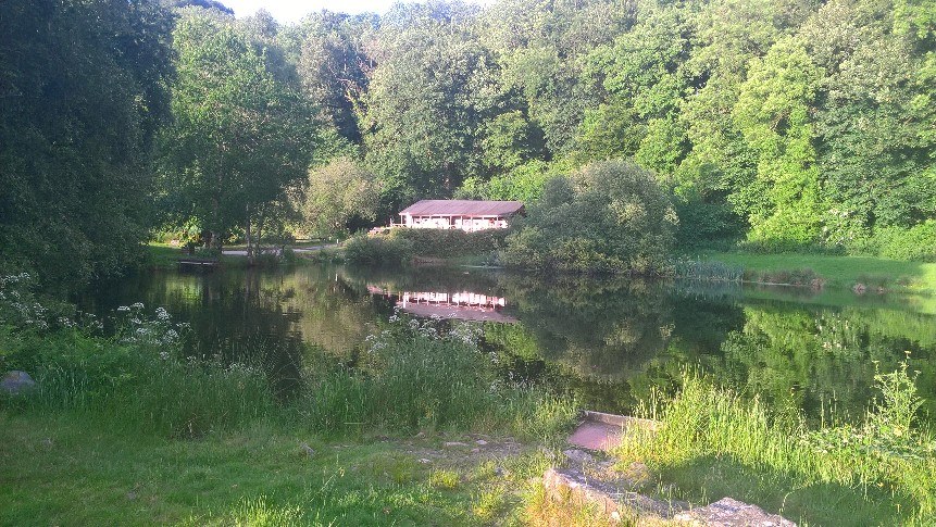 A lake fringed with trees, with a cottage on the far bank