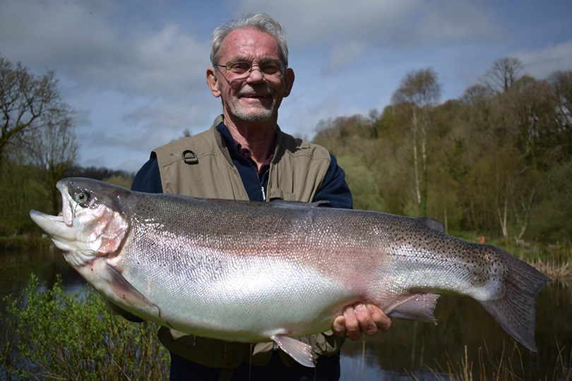 An angler holding up a large rainbow trout by the water