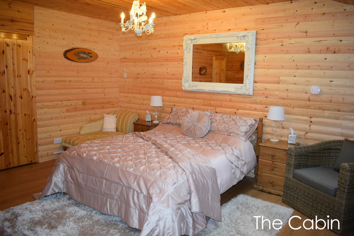 The Cabin bedroom with pine log walls, a king size bed and a mirror