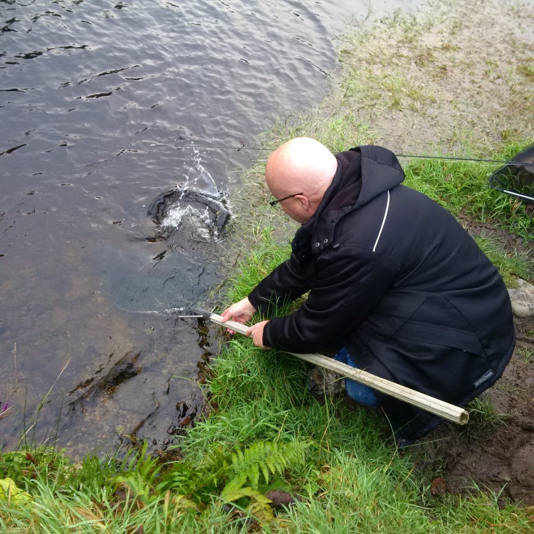 Chris Evans kneeling at the lake edge releasing a big trout