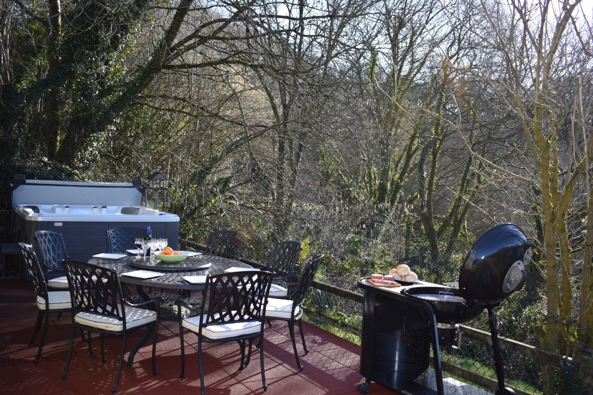 A cottage terrace above the lake with a hot tub, table, chairs and a barbecue