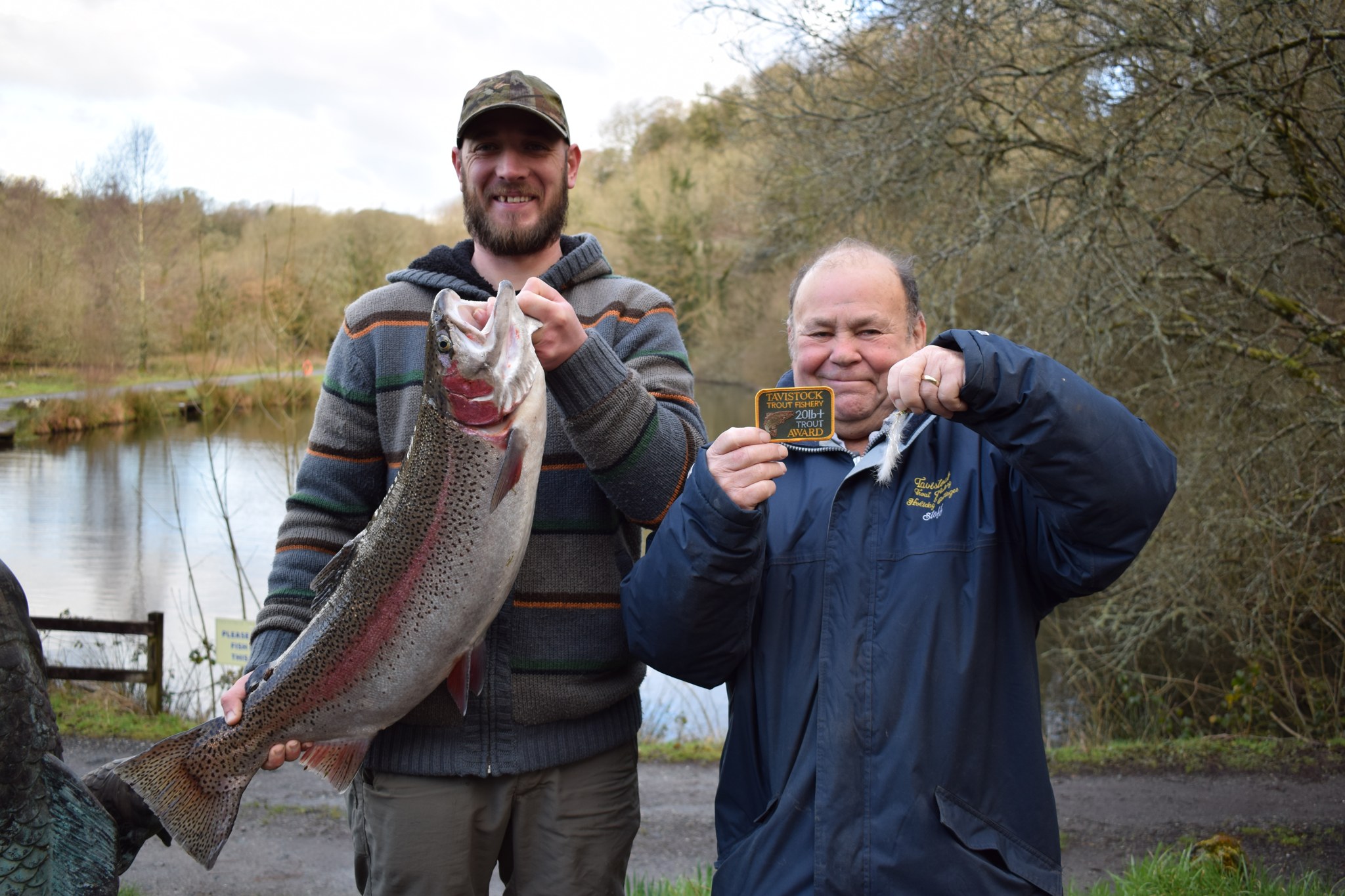 Two anglers by the lake, each holding up a big trout