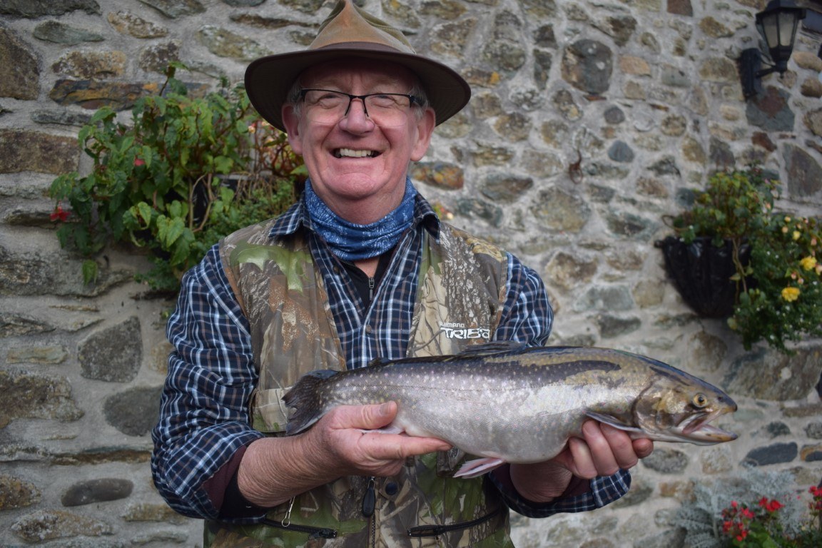 A smiling angler in a fishing waistcoat holding a trout