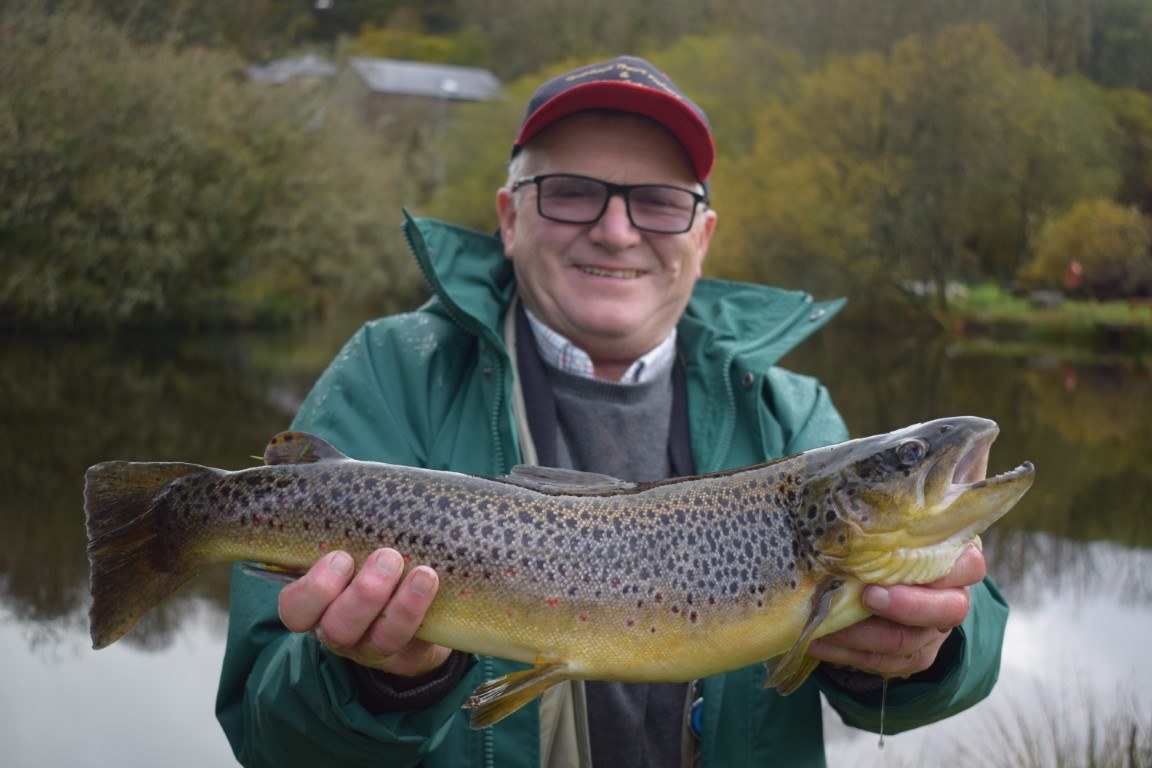 An angler in a cap holding a large brown trout by the lake