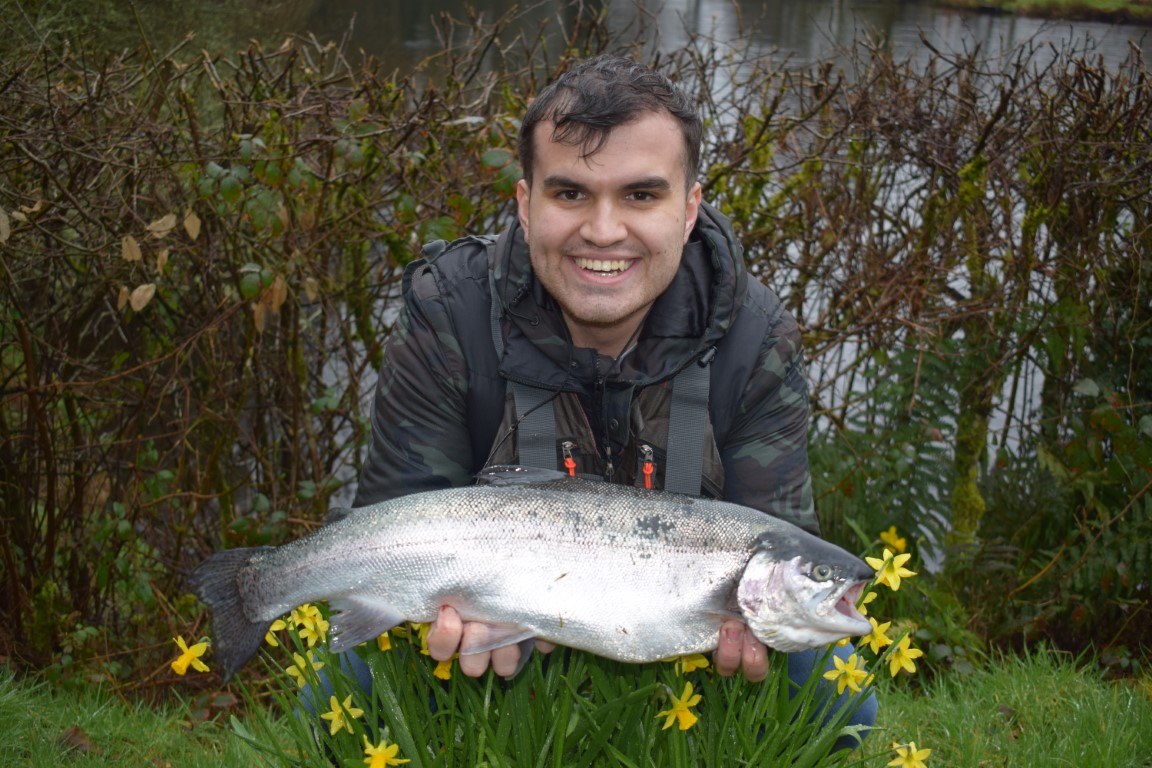 A young angler holding a silver trout among daffodils