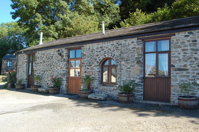 The Old Stables, a long stone barn conversion with timber doors and planters