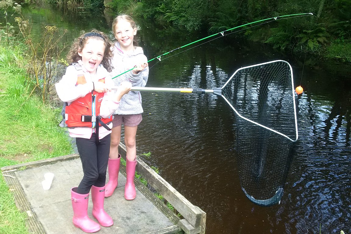 Two children on a platform at the float fishing lake, one holding a landing net